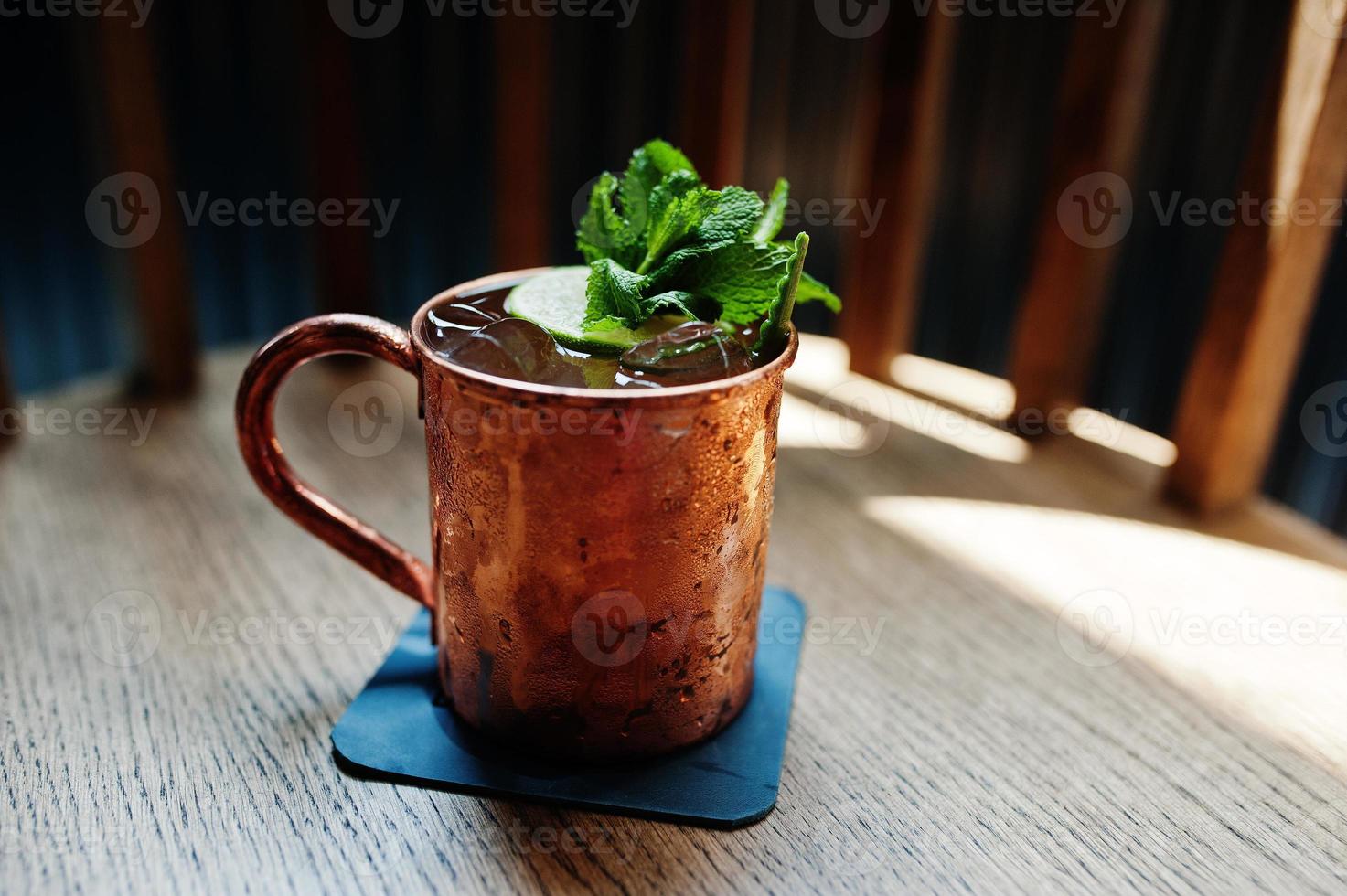 Alcoholic cocktail with ice, mint and lime in bronze cup on bar table. photo