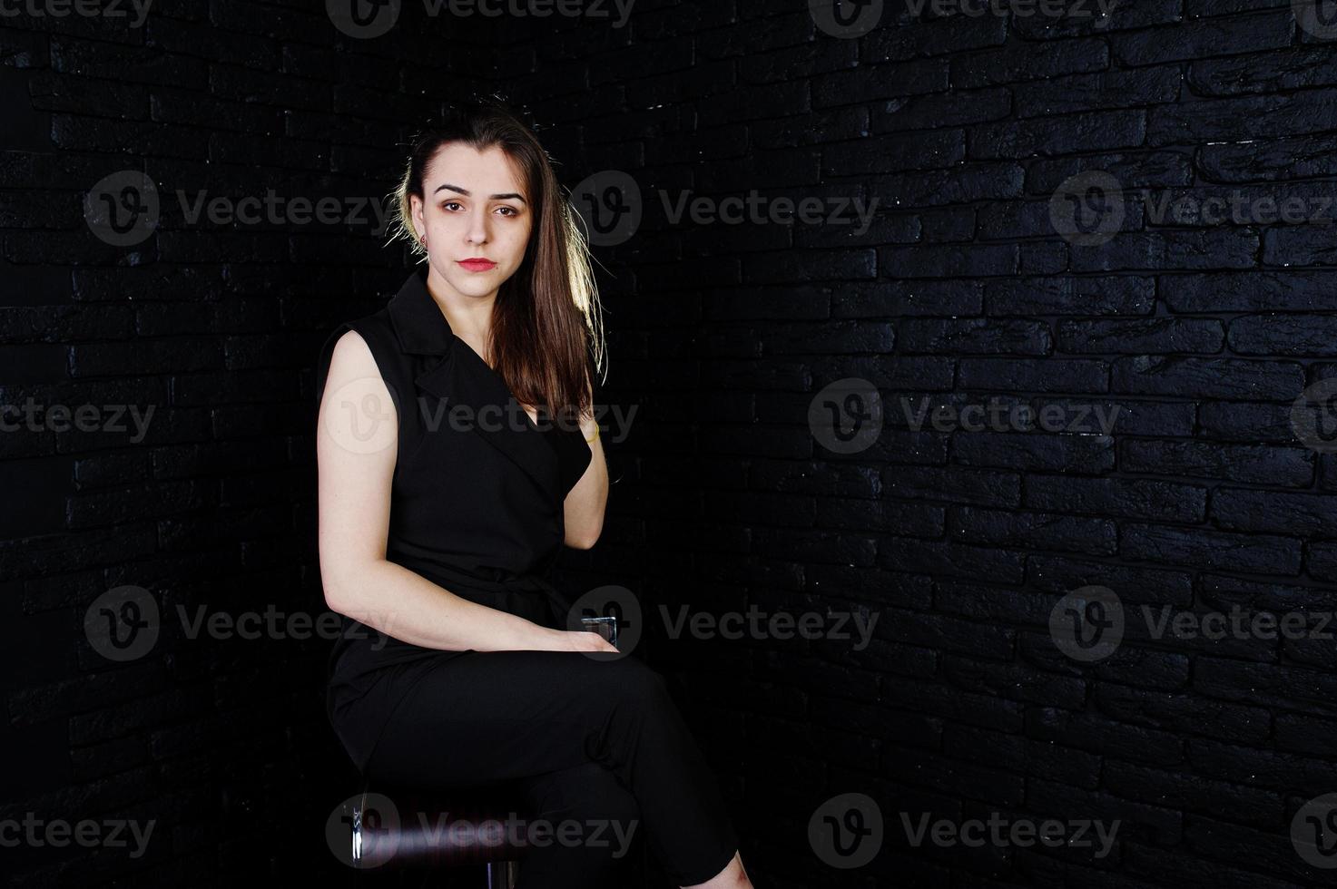 Portrait of a beautiful brunette girl in black jumpsuit sitting and posing in the studio. photo