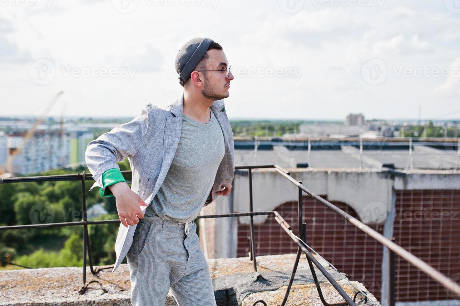 Dreamer stylish macho man in gray suit, hat and glasses posed on the roof. photo