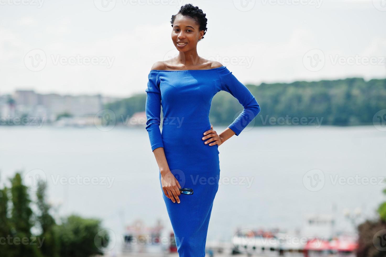 chica rizada afroamericana posó en la calle de la ciudad con vestido azul. foto