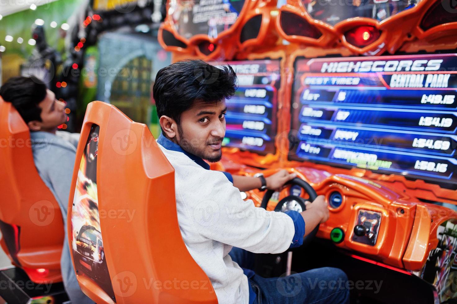 Two asian guys compete on speed rider arcade game racing simulator machine. photo