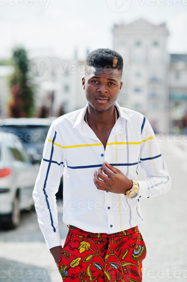 retrato de un apuesto y elegante modelo afroamericano con pantalones rojos y camisa blanca posado en la calle. foto