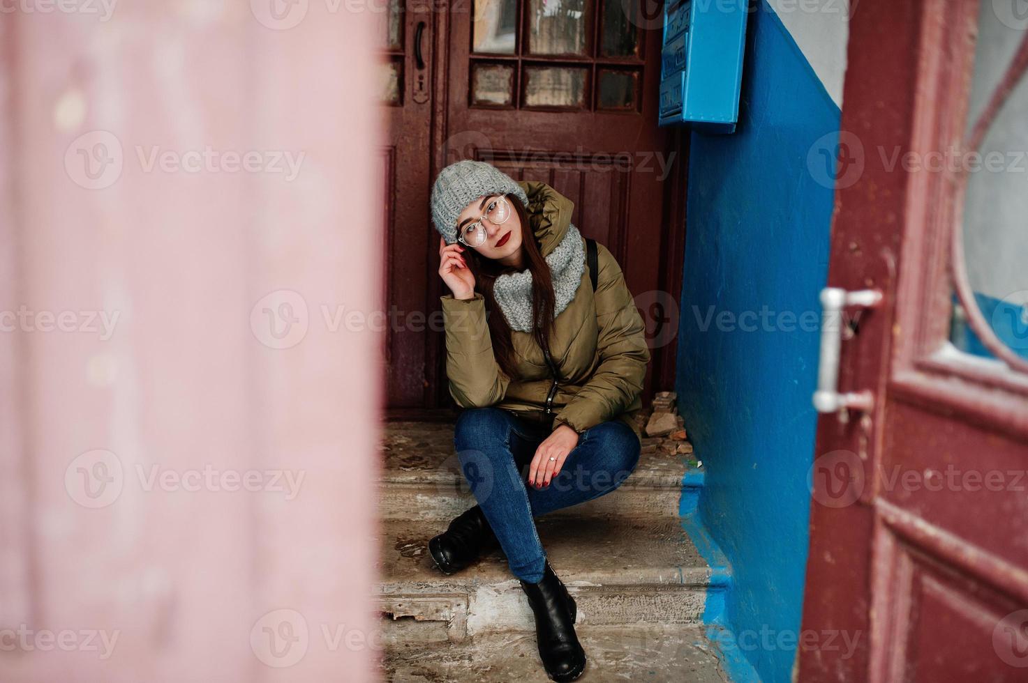 retrato de una chica morena con bufanda gris y sombrero, gafas contra la entrada. foto