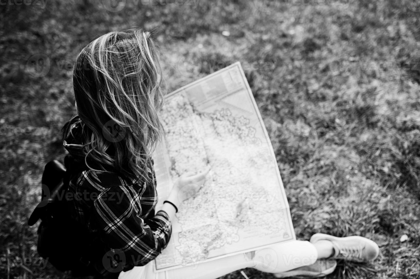 retrato de una joven y hermosa rubia positiva sentada en el suelo con un mapa en las manos en el bosque. foto