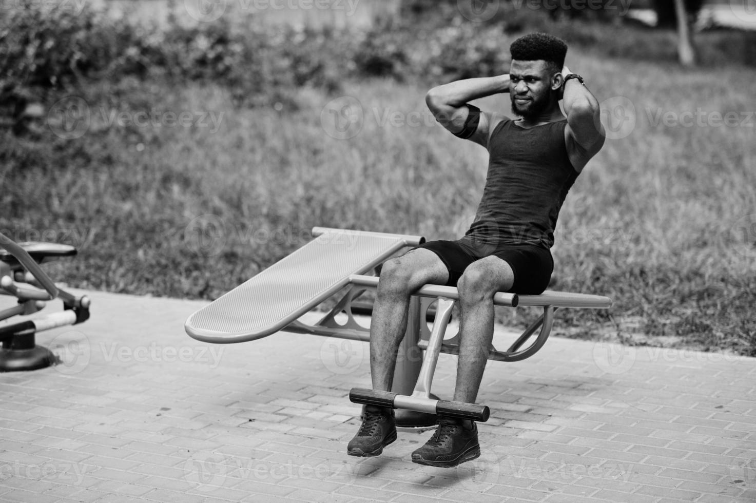 African american male athlete sport man with running sports arm case for mobile phone, doing exercises on the street workout simulators. photo