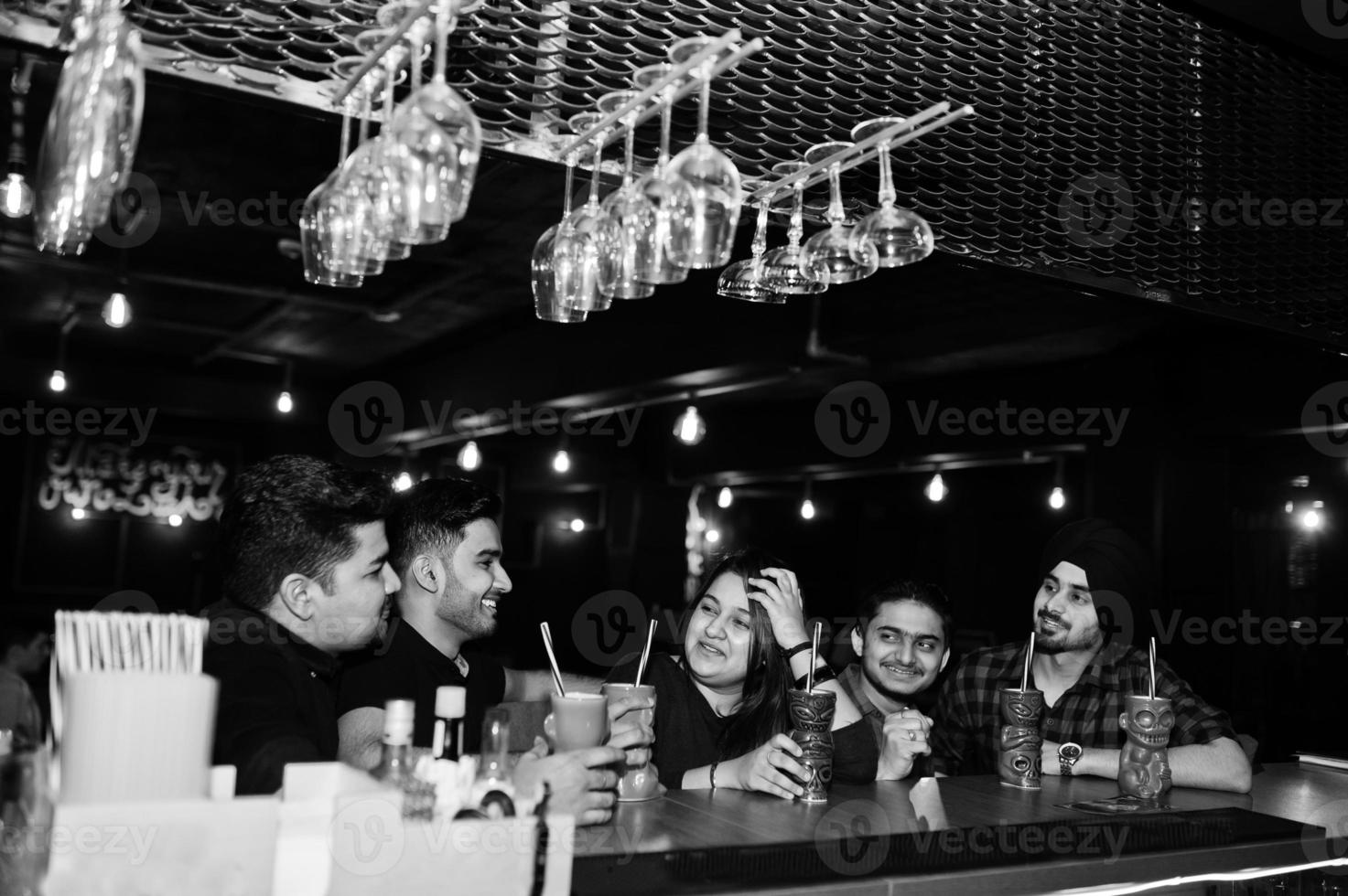 Group of indian friends having fun and rest at night club, drinking cocktails near bar counter. photo