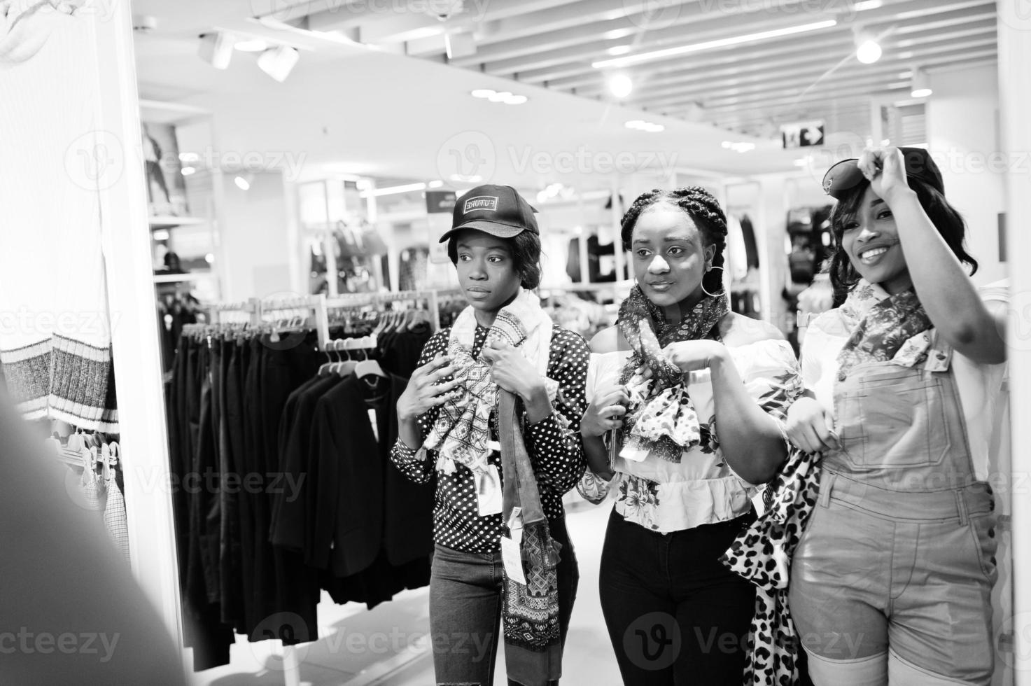 Three african woman choosing clothes at store. Shopping day. They buying caps and scarfs and looking at mirror. photo