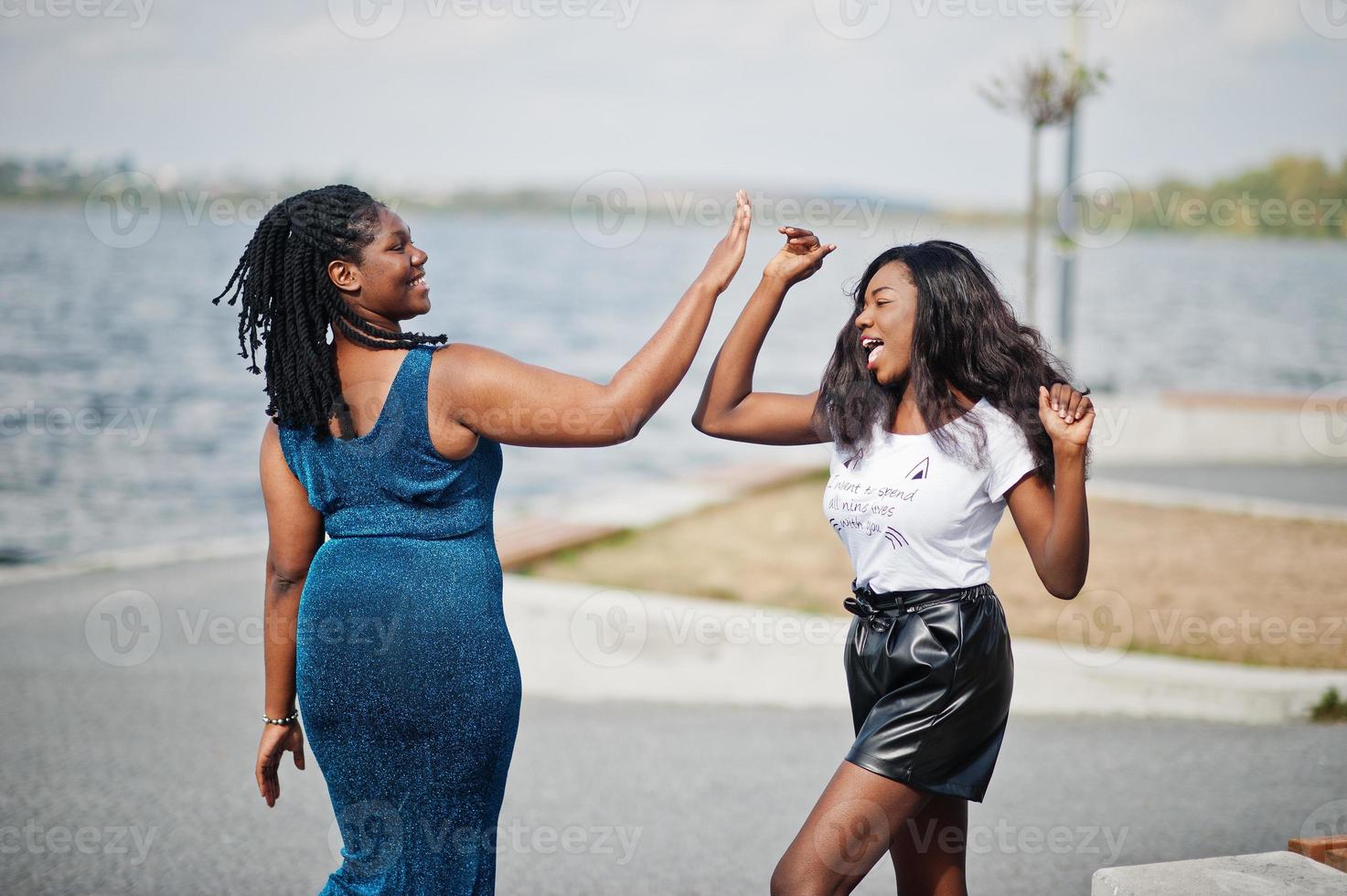 Two african american dark skinned friends female. One of them plus size model, second slim. Having fun and spending time together. Give high five each other. photo