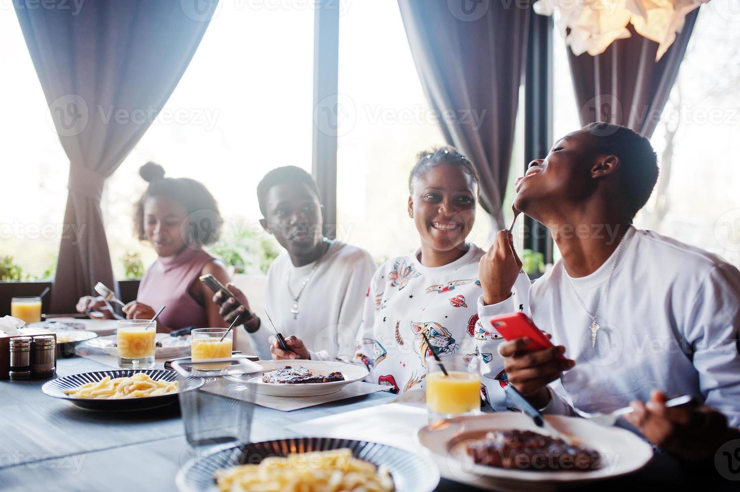 Happy african friends sitting, chatting in cafe and eat food. Group of black peoples meeting in restaurant and have dinner. photo