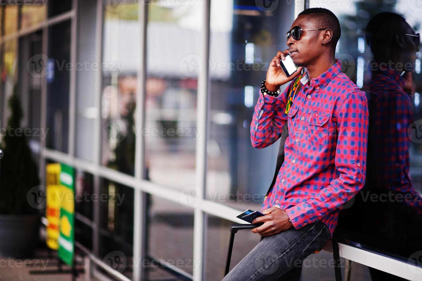 African american man in checkered shirt, with suitcase and backpack. Black man traveler against bus station. photo