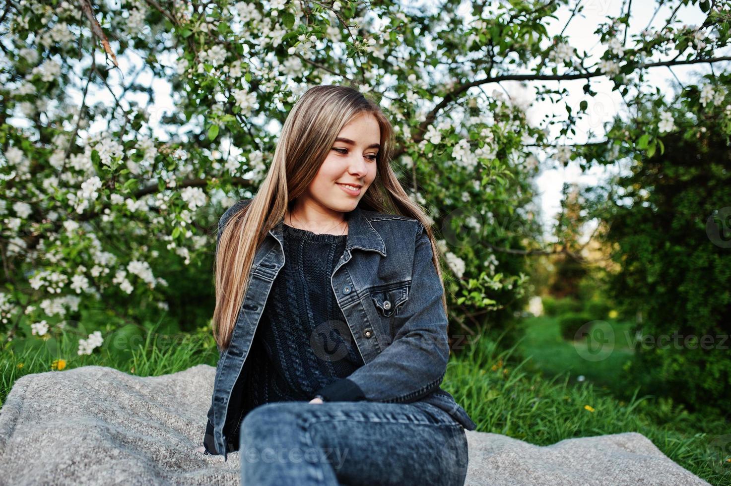 Young brunette girl at jeans sitting on plaid against spring blossom tree. photo