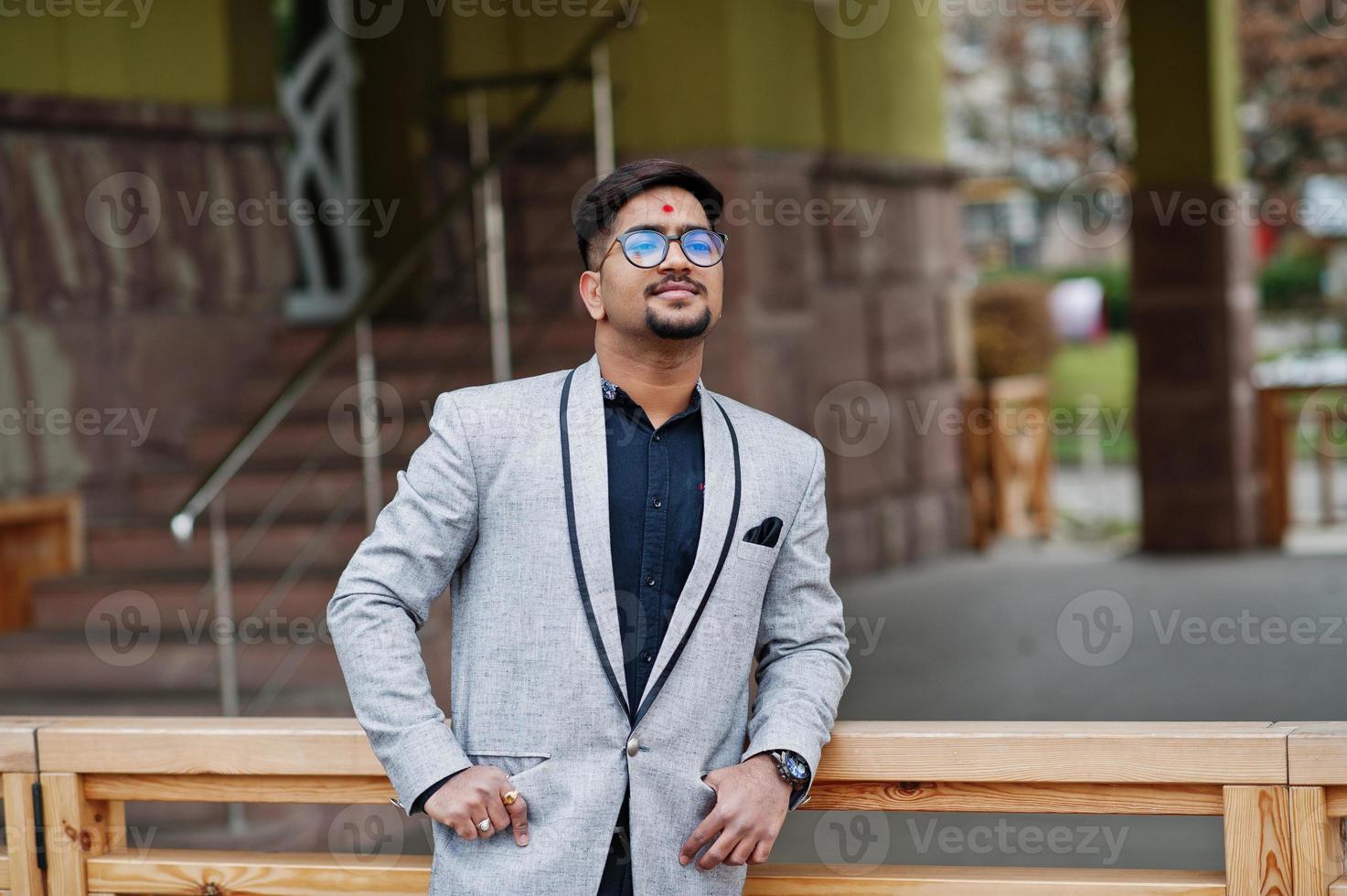 Stylish indian man with bindi on forehead and glasses, wear on gray suit posed outdoor. photo