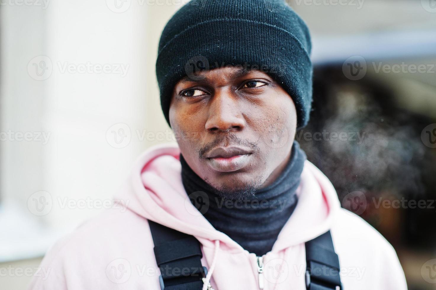 Close up head of stylish urban style african american man in pink hoodie and black hat posed. Frozen breath. photo