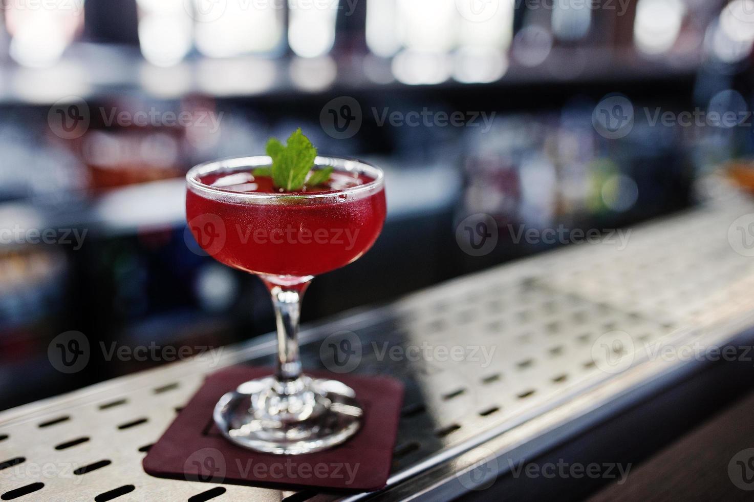 Alcoholic red cocktail with mint on bar table. photo