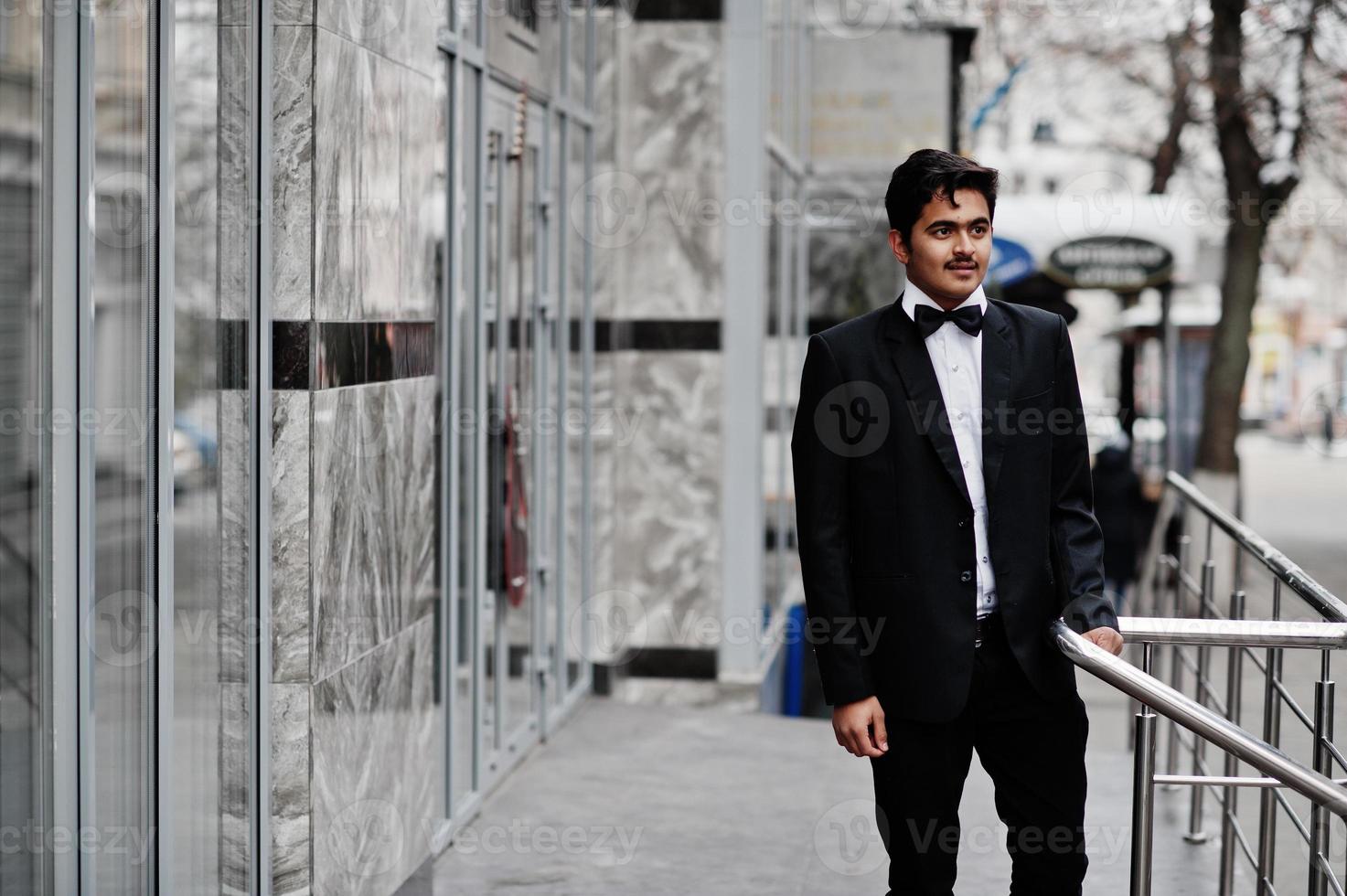 Young indian man on black suit and bow tie posed outdoor. photo