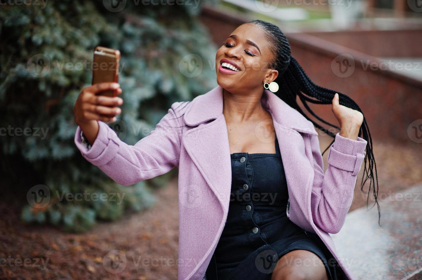 Young stylish beautiful african american woman in street, wearing fashion outfit coat, with mobile phone. photo