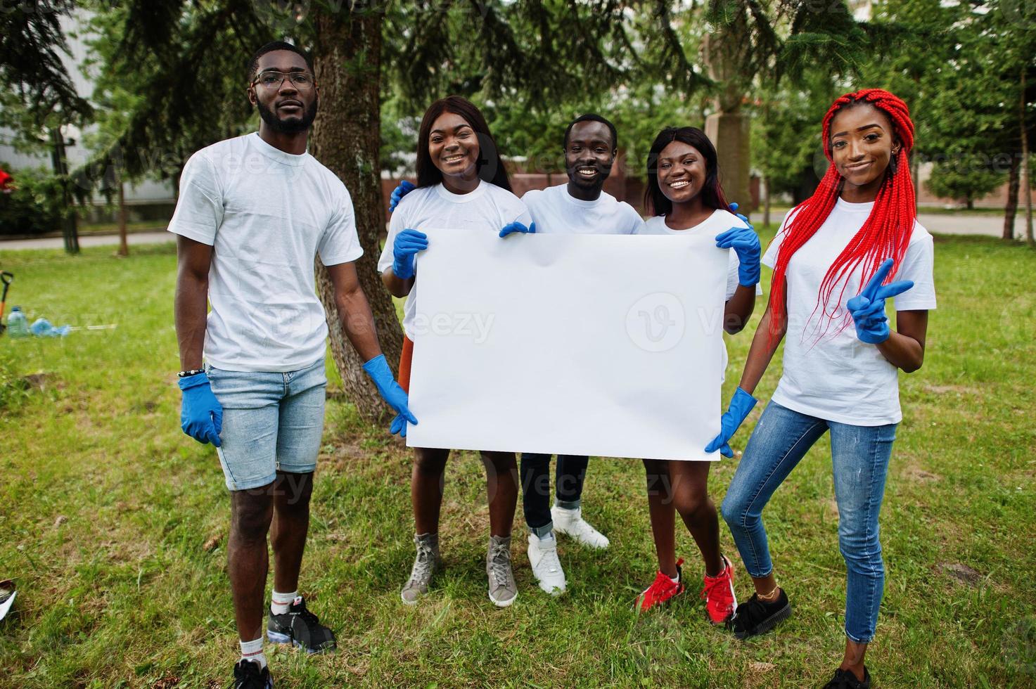 Group of happy african volunteers hold empty blank board in park. Africa volunteering, charity, people and ecology concept. Free space for your text. photo