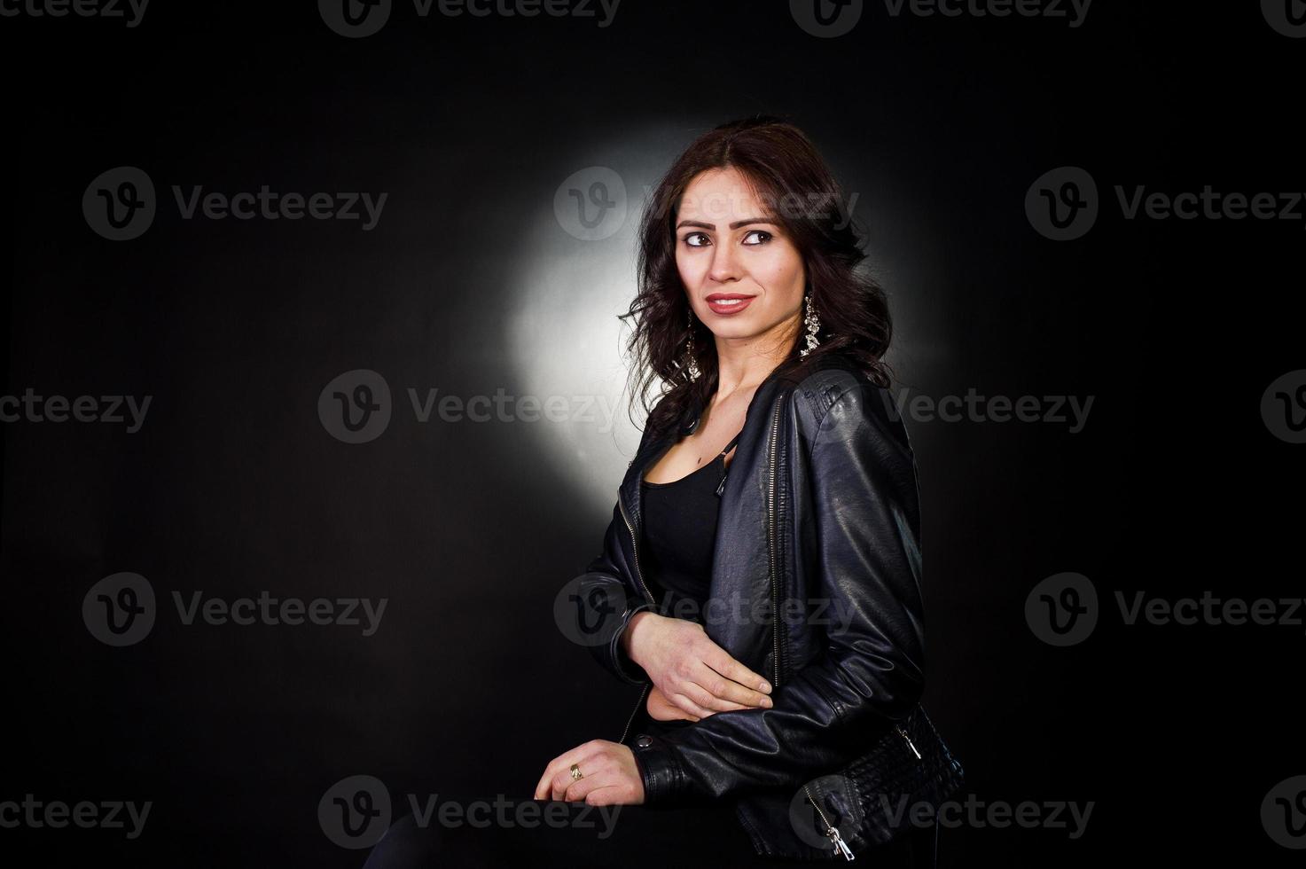 Studio portrait of sexy brunette girl in black leather jacket against black background. photo