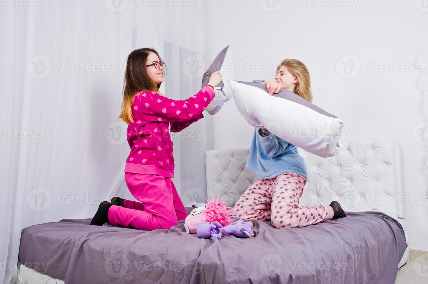 Two friends girls in pajamas having fun on bed at room. photo