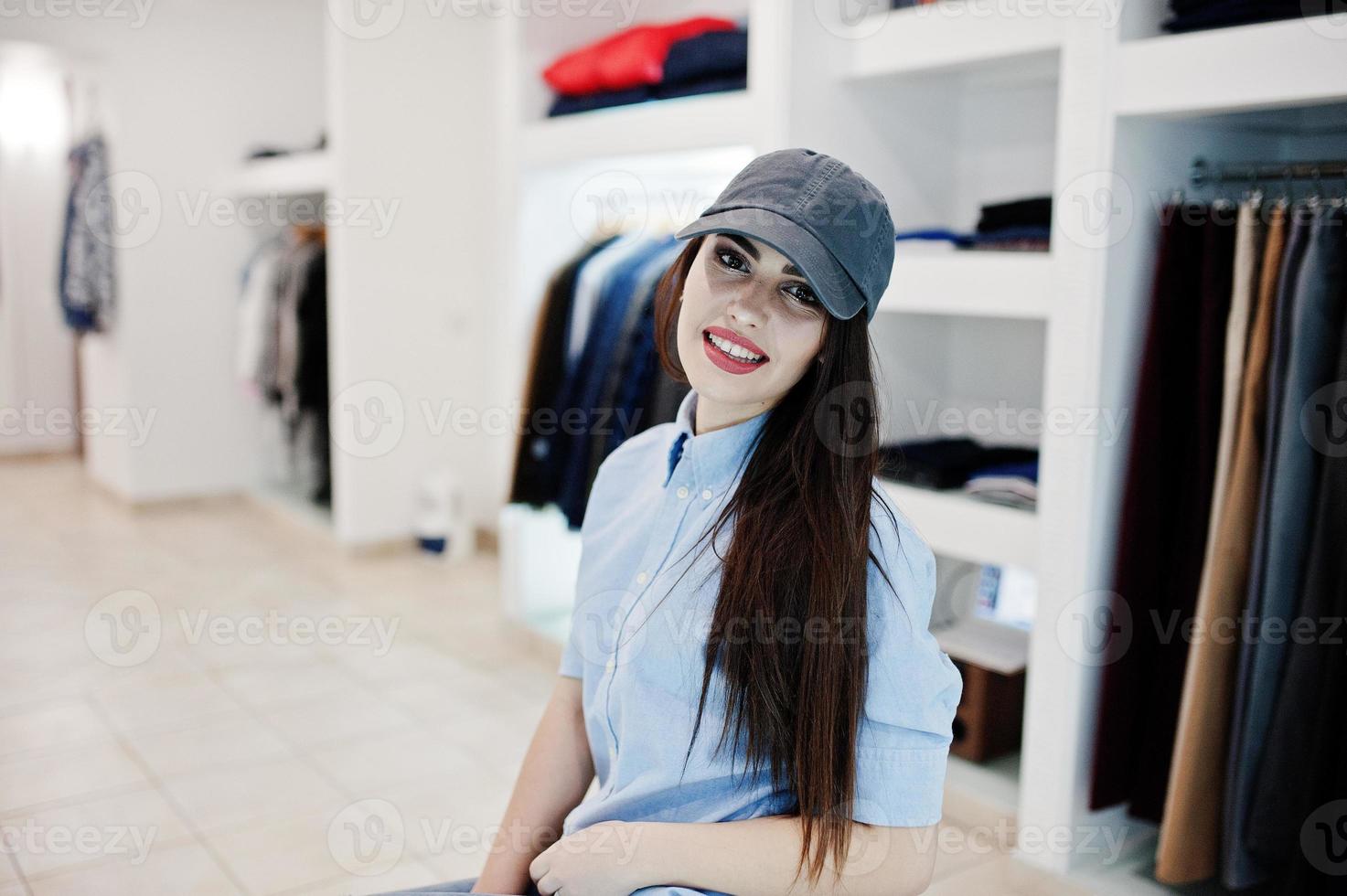 hermosa chica morena en la boutique de la tienda de ropa en ropa casual y gorra. foto