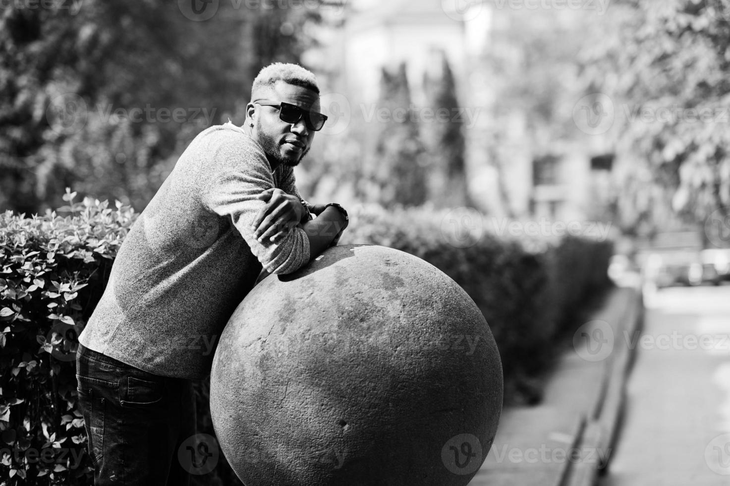 Elegante chico afroamericano con suéter gris y gafas de sol negras posadas en la calle. chico negro de moda. foto