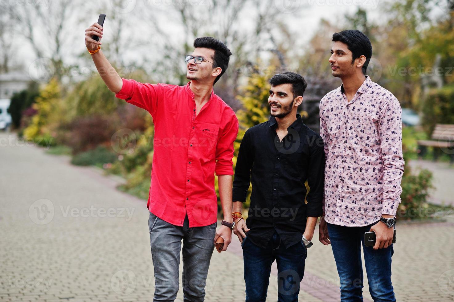 Three indian guys students friends walking on street and makes selfie on mobile phone. photo