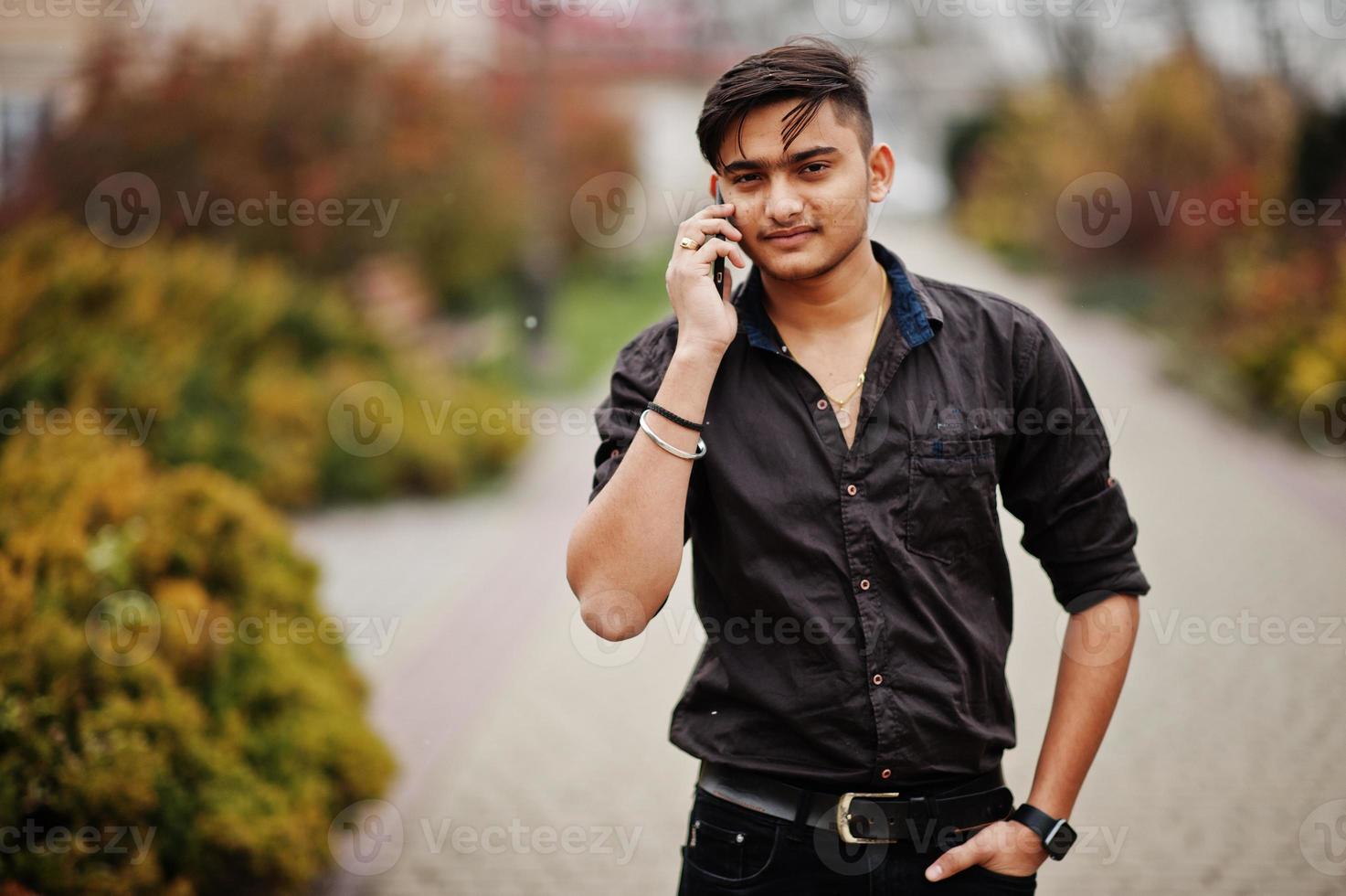 hombre indio con camisa marrón posó al aire libre y hablando por teléfono móvil. foto