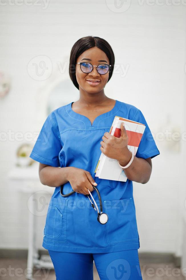 Portrait of happy female african american young doctor pediatrician in blue uniform coat and stethoscope with books at hands. Healthcare, medical, medicine specialist - concept. photo
