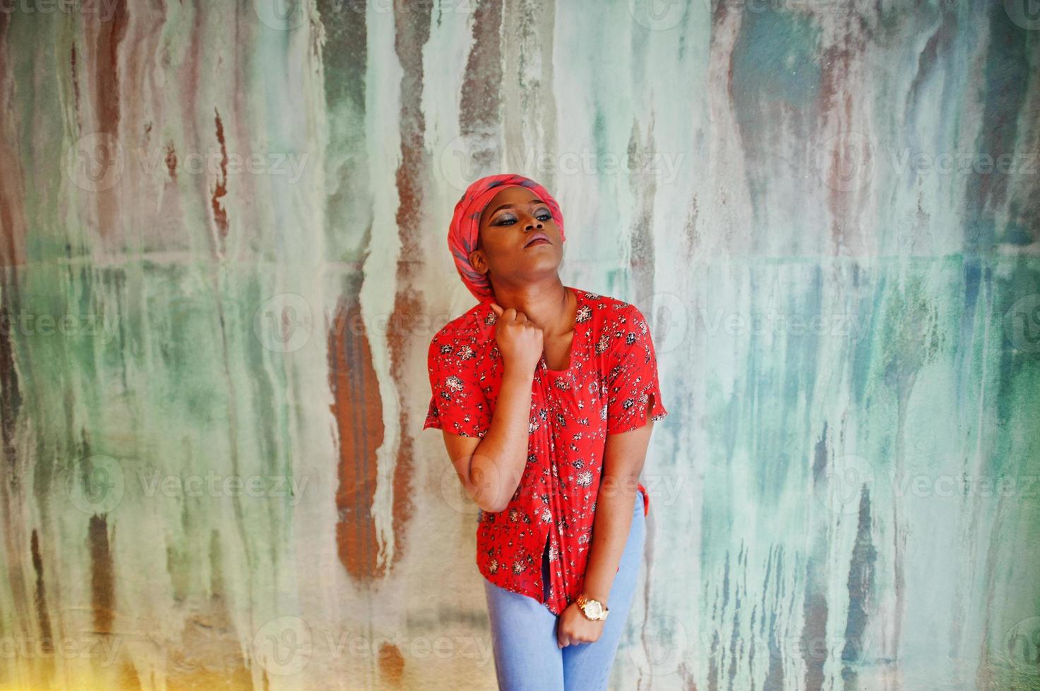 Stylish african woman in red shirt and hat posed against wall. photo