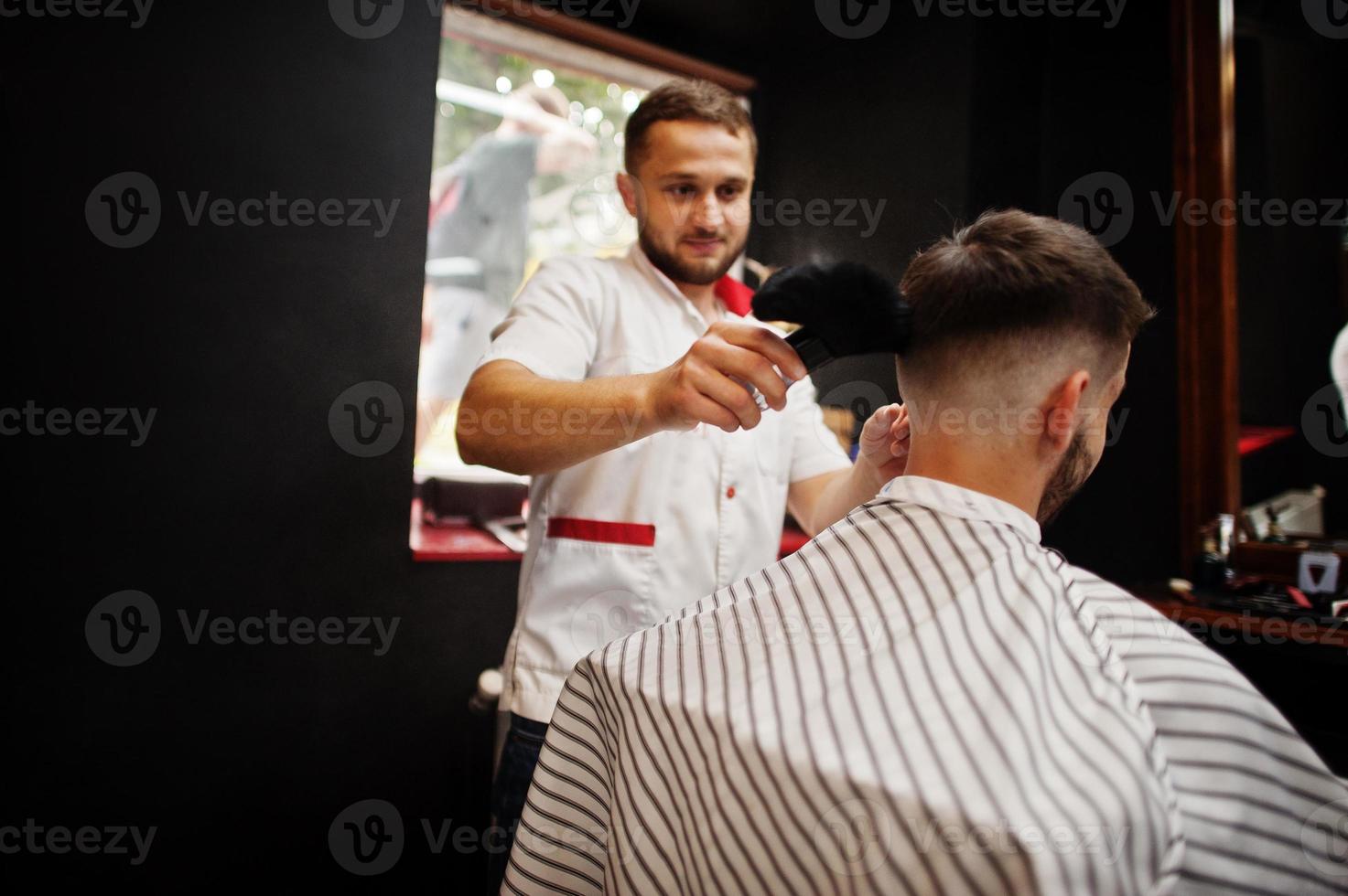 un joven barbudo que se corta el pelo con un peluquero mientras se sienta en una silla en la barbería. alma de barbero. foto