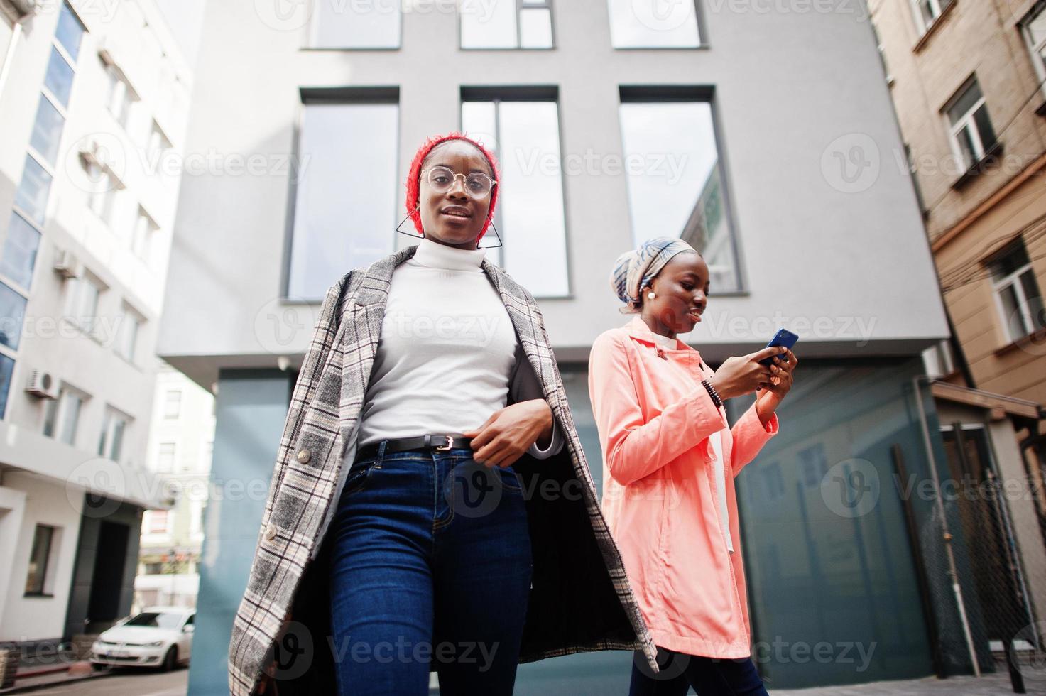 Two young modern fashionable, attractive, tall and slim african muslim womans in hijab or turban head scarf and coat posed with mobile phones. photo