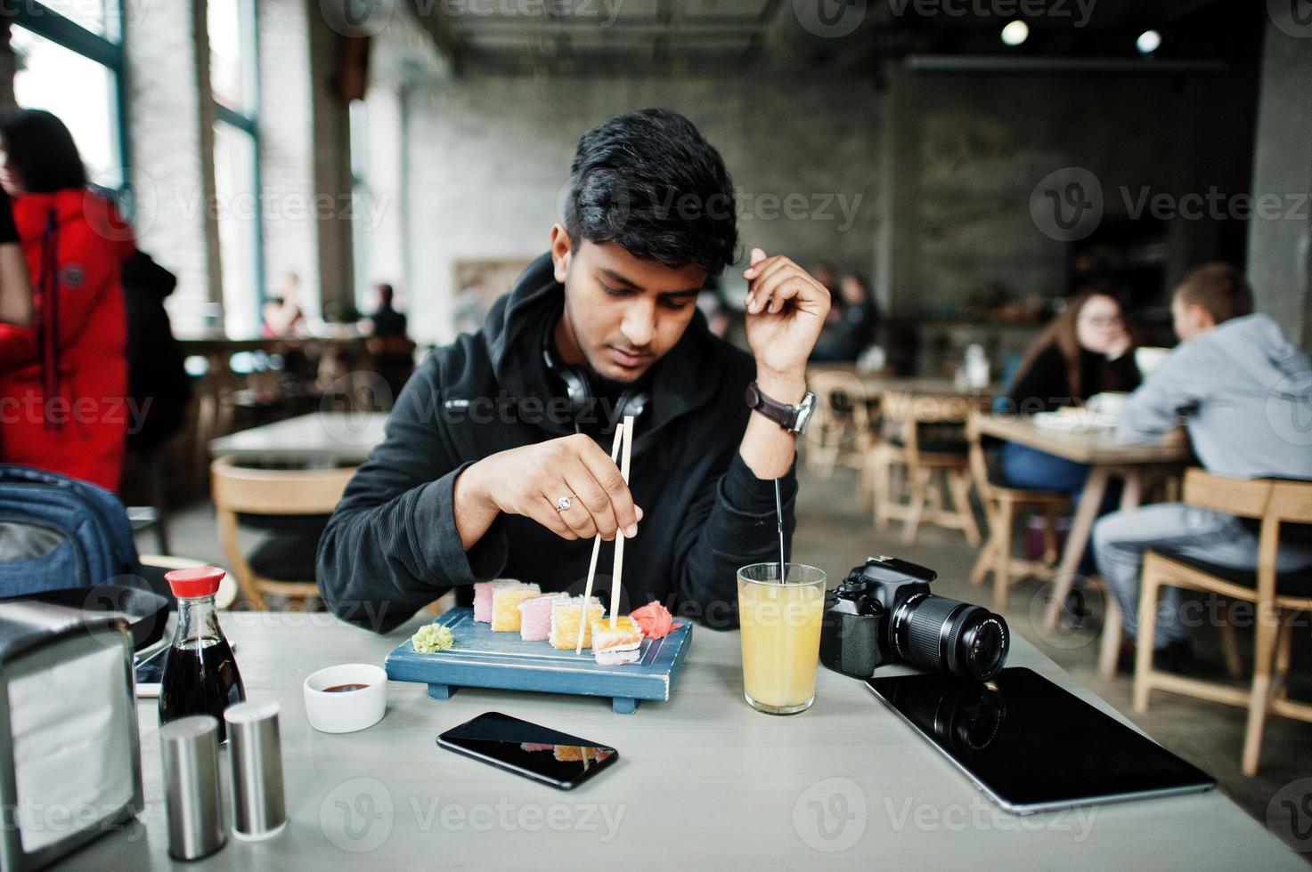 Casual and stylish young asian man with earphones at cafe eating sushi. photo