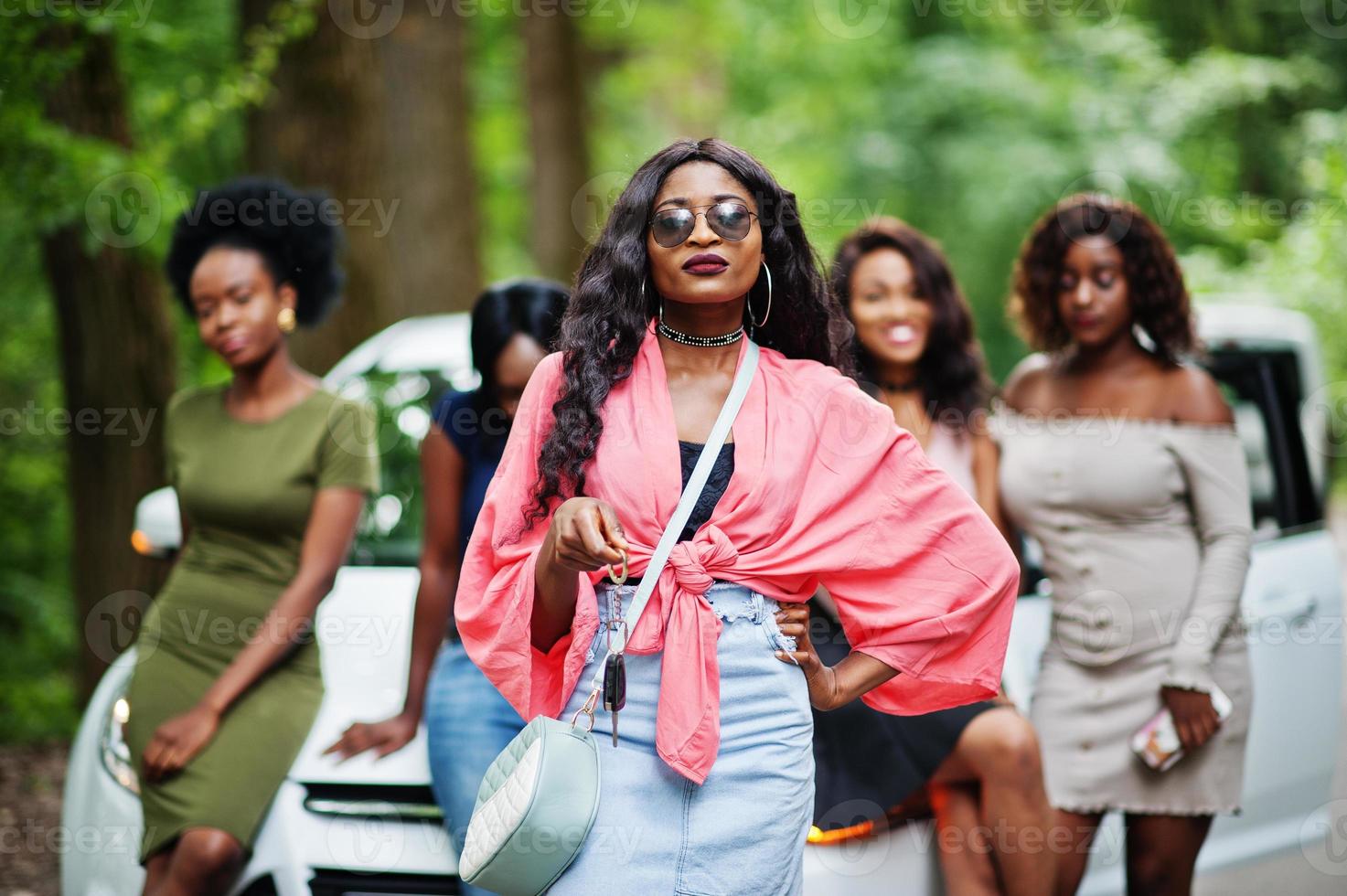 Group of five happy african american girls posed against car, one of them show keys. photo