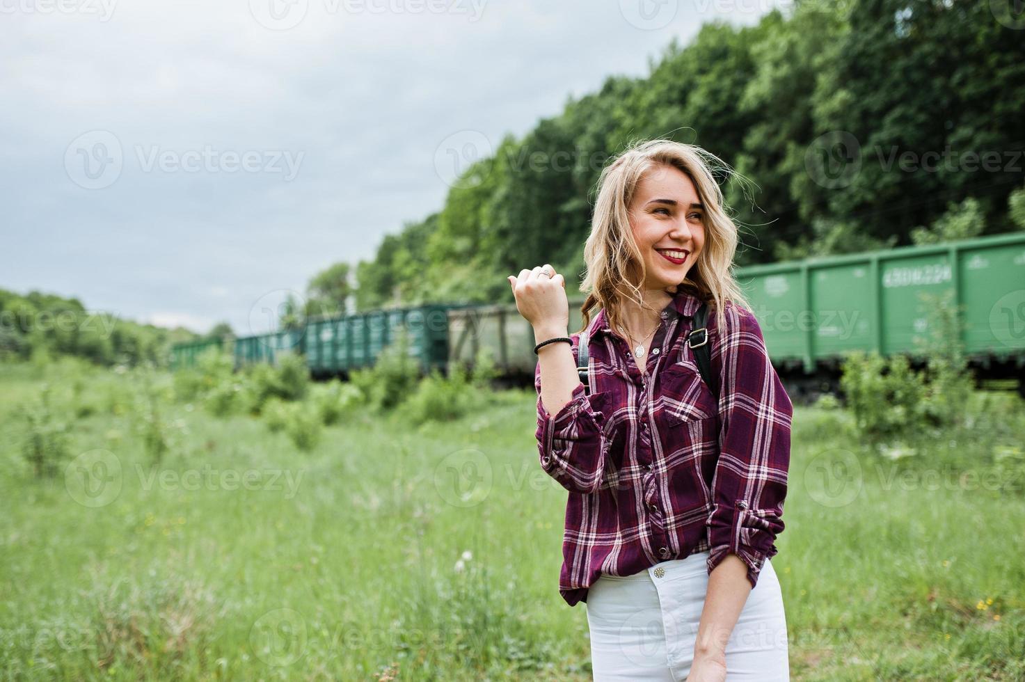 retrato de una joven rubia con camisa de tartán al lado del tren con un mapa. foto