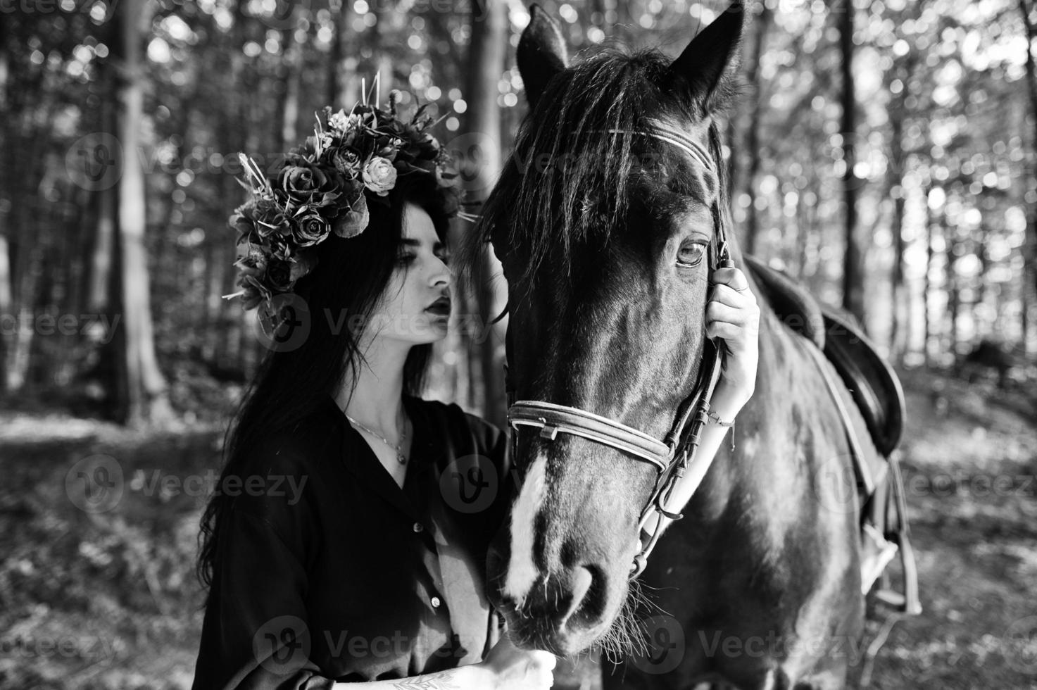 Mystical girl in wreath wear in black with horse in wood. photo