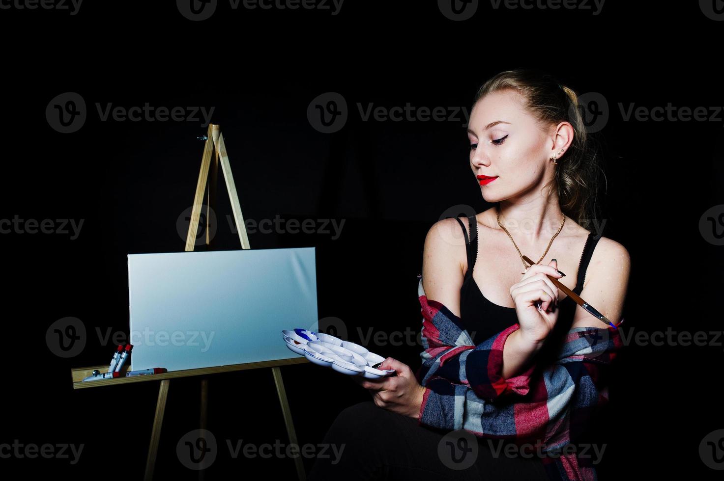 Beautiful woman artist painter with brushes and oil canvas posing in studio isolated on black. photo