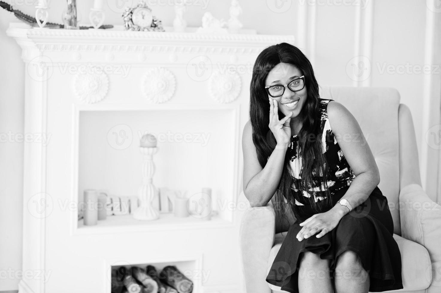 Pretty african american woman in eyeglasses posed in room, sitting on yellow chair. photo