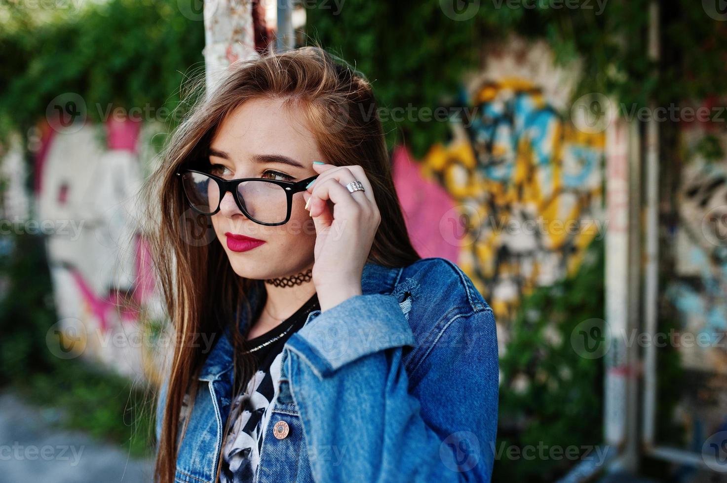 Stylish casual hipster girl in jeans wear and glasses against large graffiti wall. photo