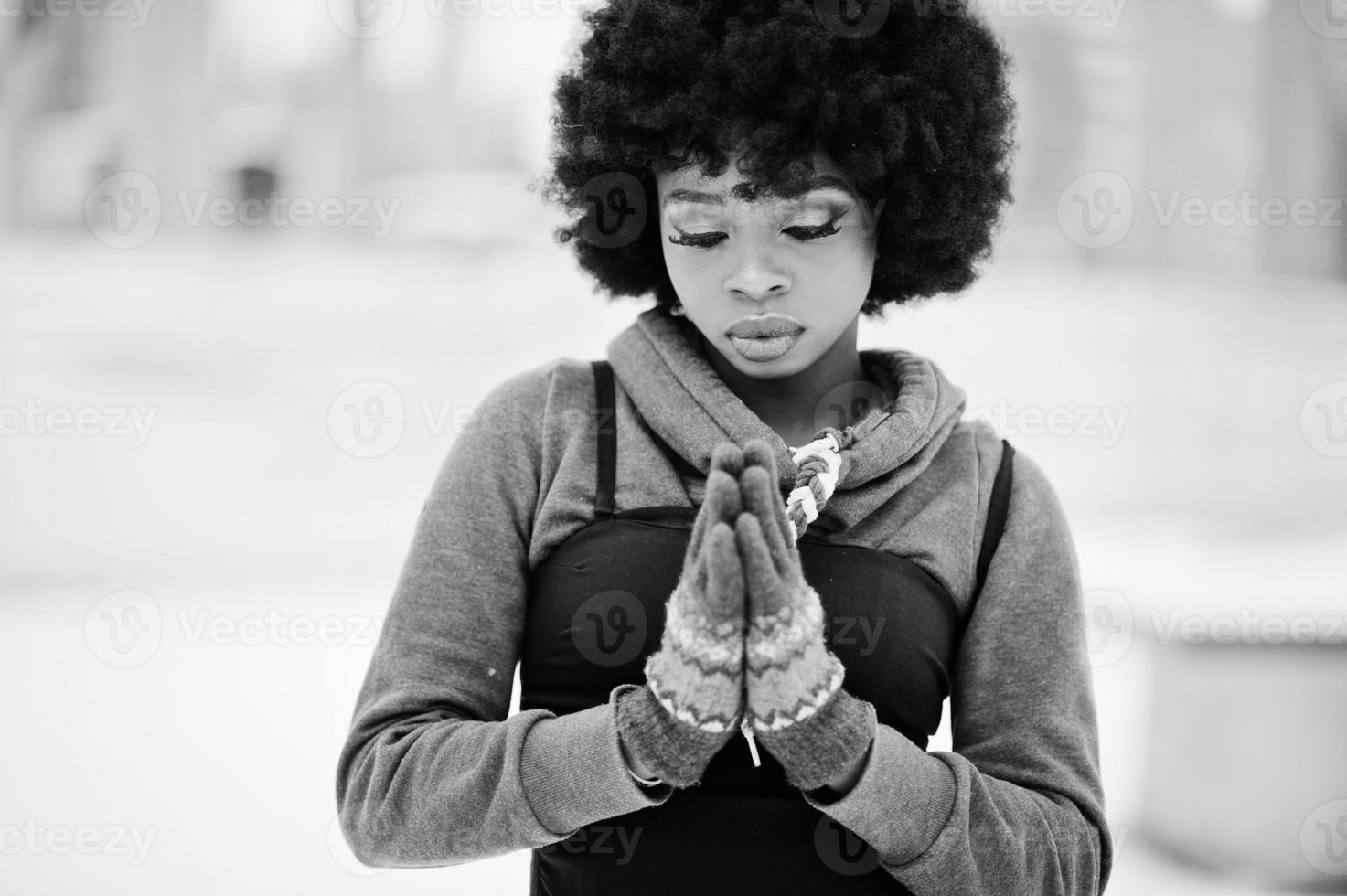 Curly hair african american woman with gloves, hands together like praying, posed at winter day. photo