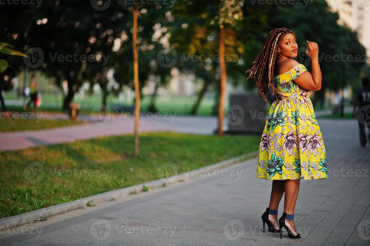 Cute small height african american girl with dreadlocks, wear at coloured yellow dress, posed at sunset. photo