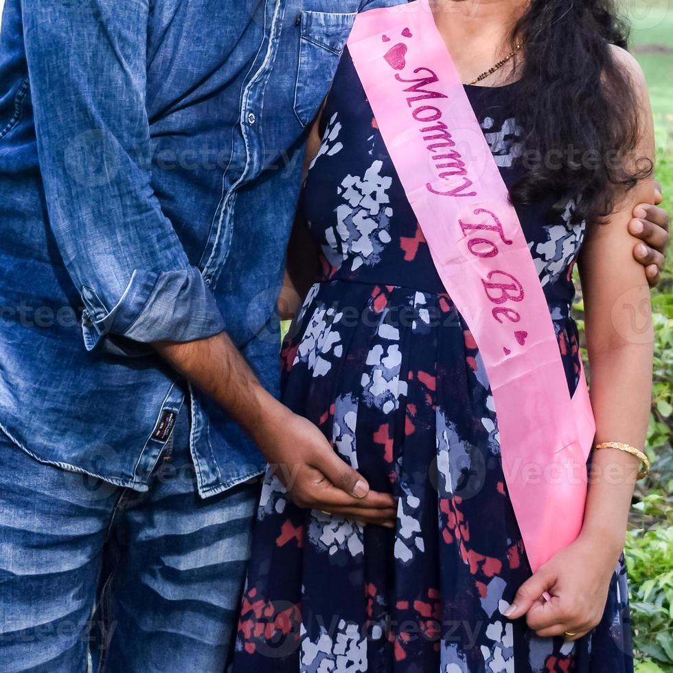 Indian couple posing for maternity baby shoot. The couple is posing in a lawn with green grass and the woman is falunting her baby bump in Lodhi Garden in New Delhi, India photo