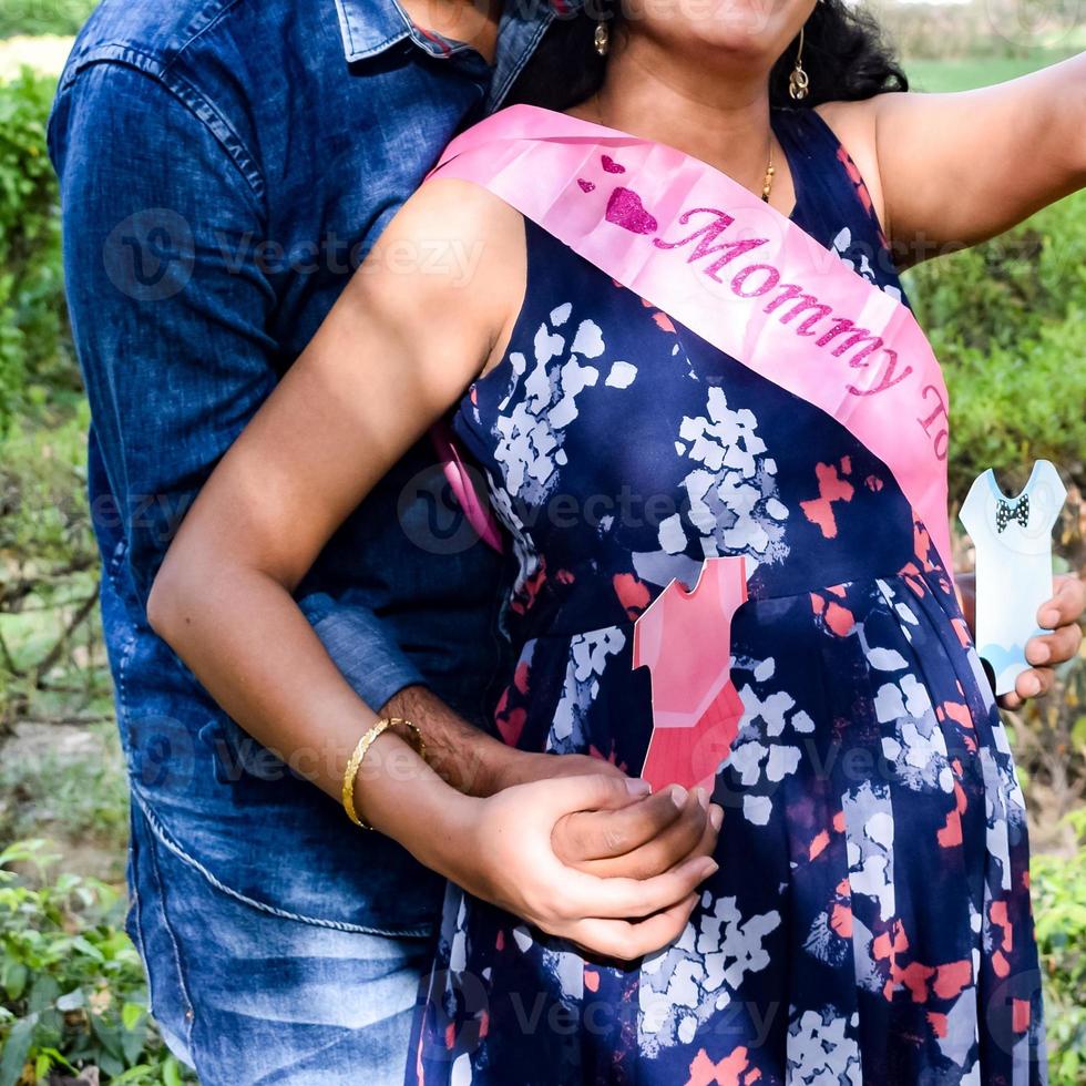 Indian couple posing for maternity baby shoot. The couple is posing in a lawn with green grass and the woman is falunting her baby bump in Lodhi Garden in New Delhi, India photo