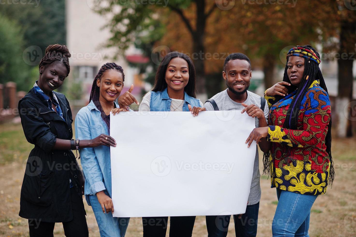 Group of five african college students on campus at university yard hold empty white blank. Free space for your text. Black afro friends studying. photo