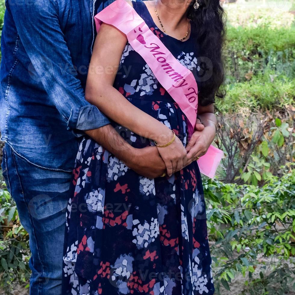 Indian couple posing for maternity baby shoot. The couple is posing in a lawn with green grass and the woman is falunting her baby bump in Lodhi Garden in New Delhi, India photo