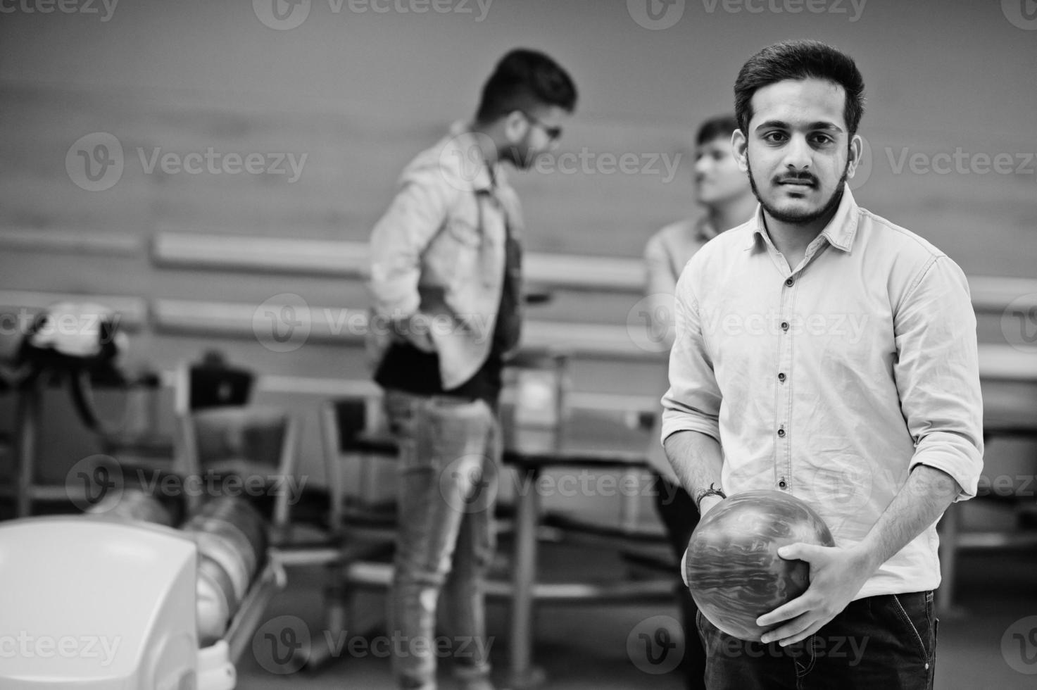 hombre del sur de asia con camisa de jeans parado en una bolera con pelota en las manos. el tipo se está preparando para un lanzamiento. foto