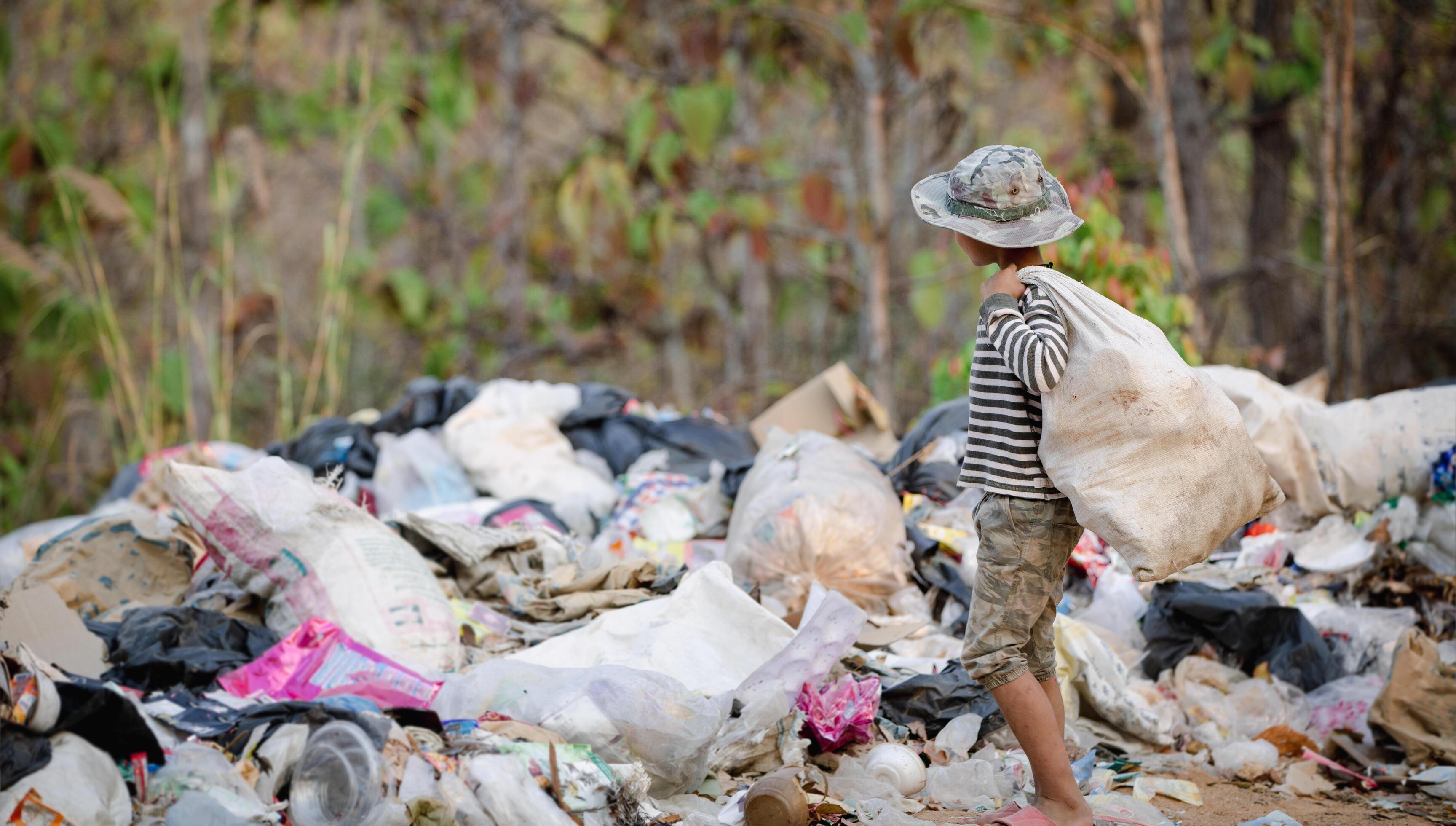 A poor Indian rag picker boy carrying a huge load of garbage collected