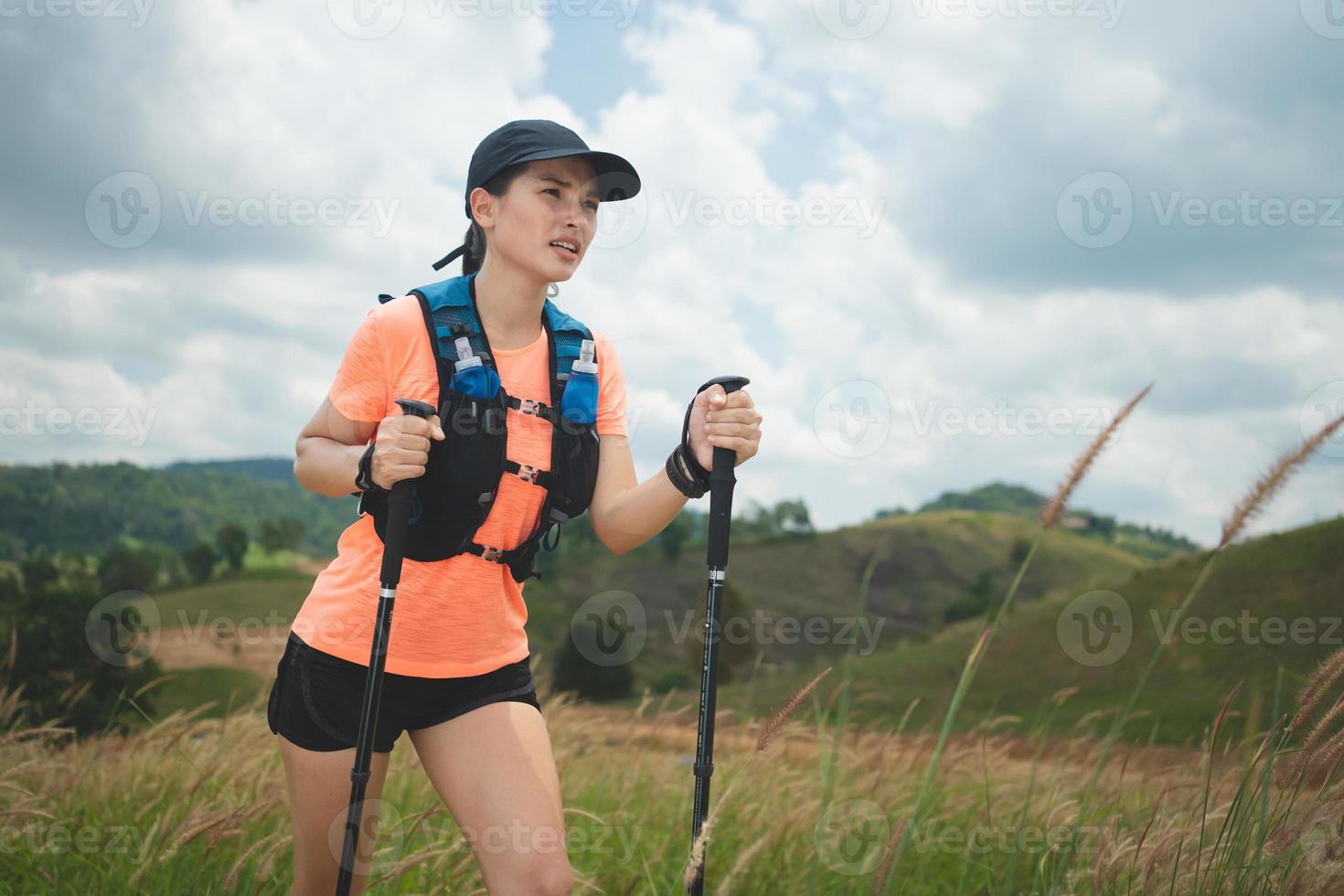 Young women active trail running across a meadow on a grassy trail high in the mountains in the afternoon with trekking pole photo