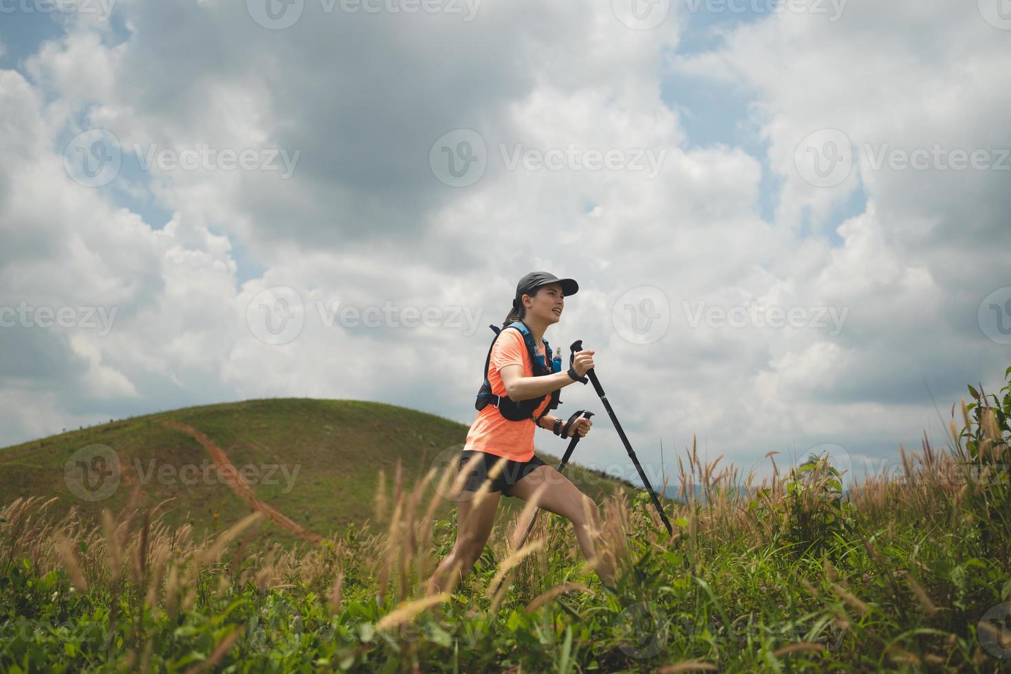 Young women active trail running across a meadow on a grassy trail high in the mountains in the afternoon with trekking pole photo