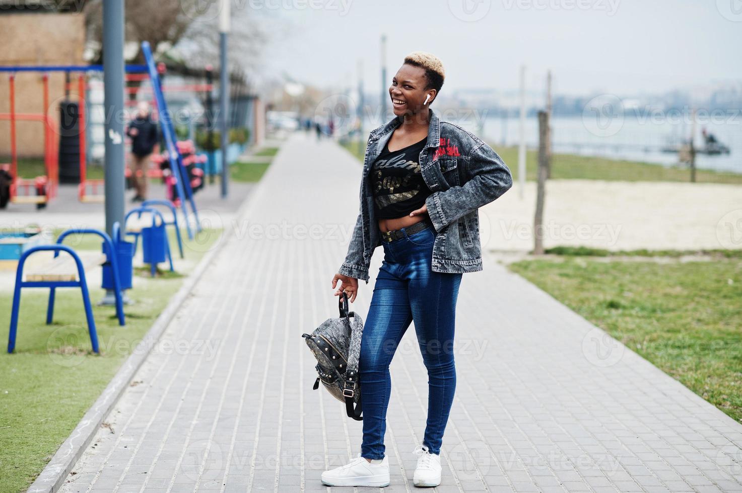 Young millennial african american girl in city. Happy black woman with wireless earphones. Generation Z concept. photo