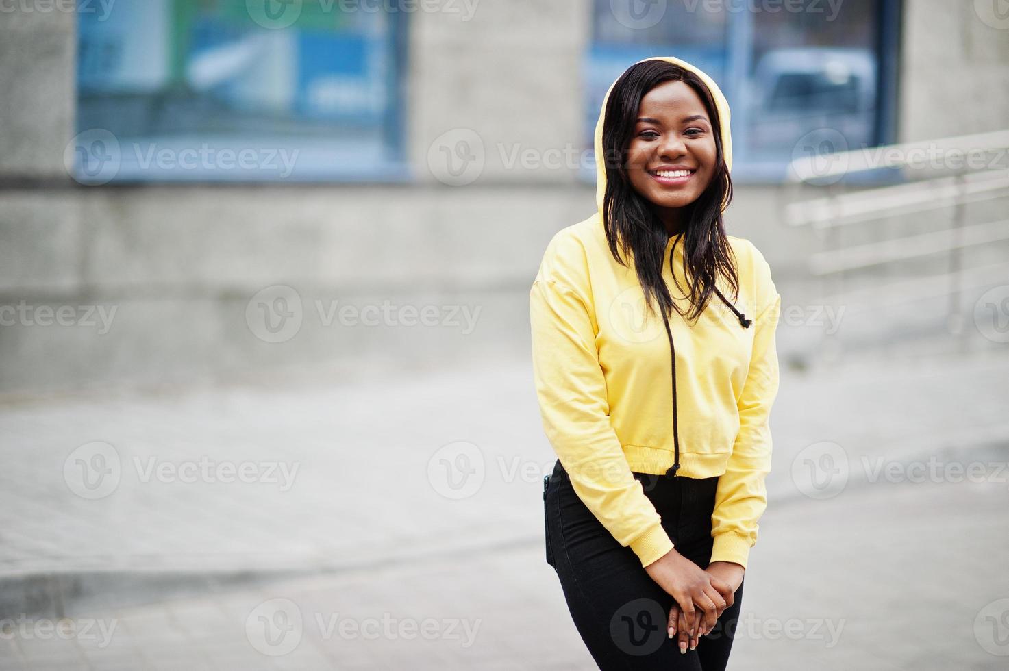 Hipster african american girl wearing yellow hoodie posing at street. photo